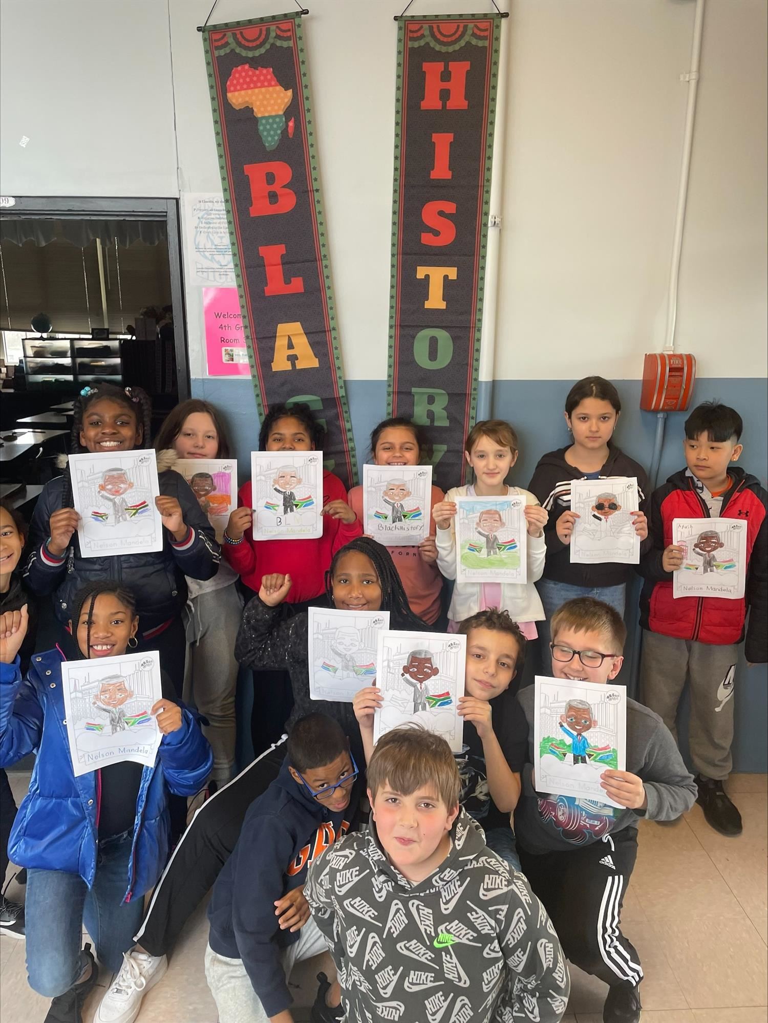 A group of students holding up completed coloring book pictures of Nelson Mandela.